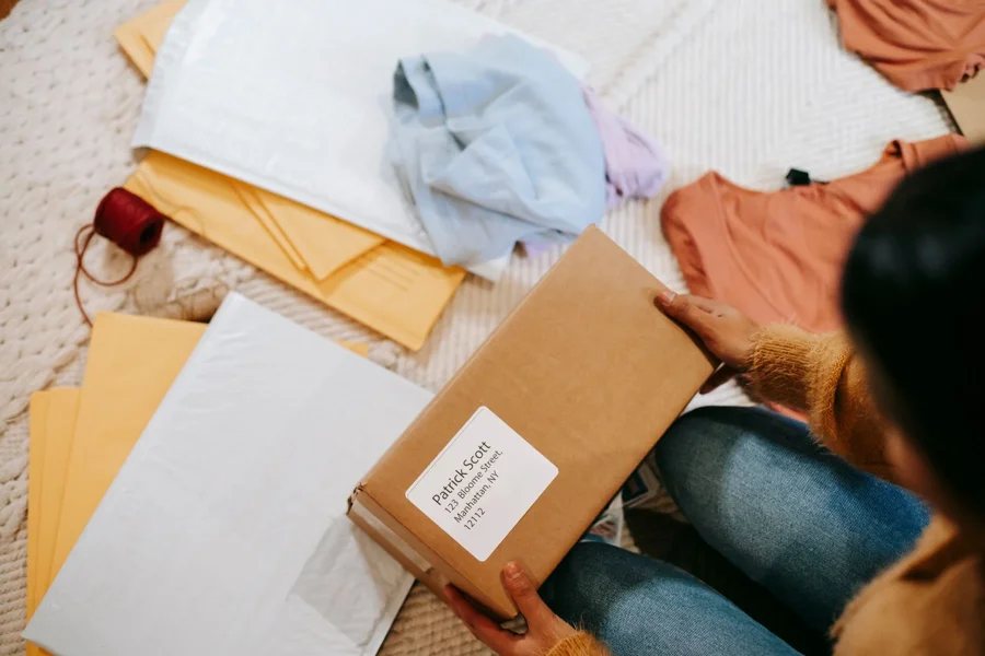 Hands checking a labelled cardboard parcel among clothing and mailing materials