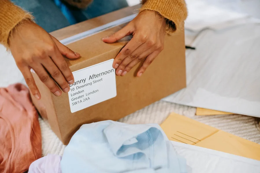 Hands closing the top of a cardboard parcel beside folded clothing